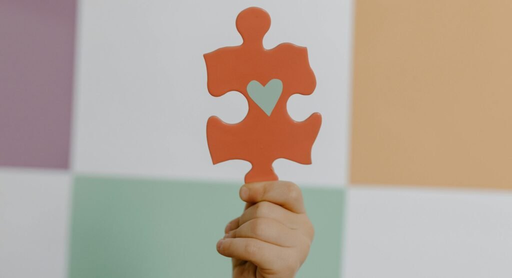 pexels photo 8386184 8386184 A hand holds a red puzzle piece with a heart, symbolizing connection and awareness.